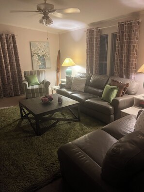 A living room with a sofa, armchair, coffee table, and a ceiling fan.