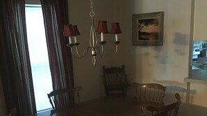 Un comedor con una mesa y sillas de madera, una araña y un cuadro en la pared.