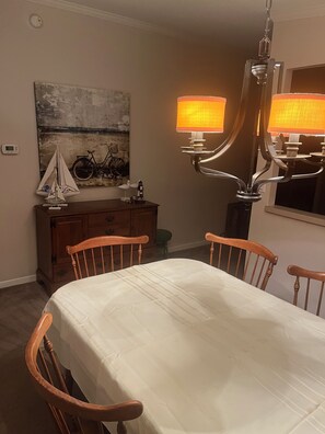 A dining room with a table, chairs, a chandelier, a painting, and a bicycle.