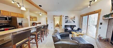 A modern kitchen with a bar area, a leather sofa, and a dining table.