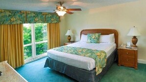 Une chambre avec un grand lit, deux tables de chevet avec des lampes, un ventilateur de plafond et une fenêtre avec des rideaux.