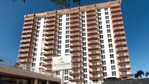Un grand hôtel avec de nombreux balcons, une enseigne indiquant qu’il s’agit du Fort Lauderdale Beach Resort, et un ciel bleu clair en arrière-plan.