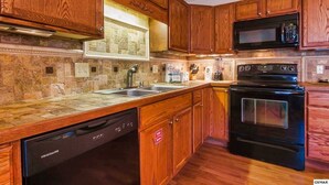 A kitchen with wooden cabinets, a dishwasher, a microwave, and an oven. - Pappy’s Hideaway (Gatlinburg)