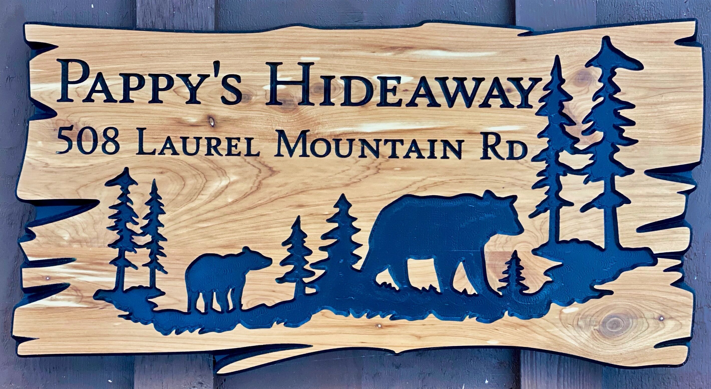 Une enseigne en bois portant l’inscription « Pappy’s Hideaway, 508, route Laurel Mountain » et représentant en silhouette un ours, un chien et des arbres.
