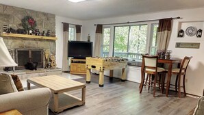 A living room with a fireplace, television, foosball table, and a dining area with a table and chairs. - Pappy’s Hideaway (Gatlinburg)
