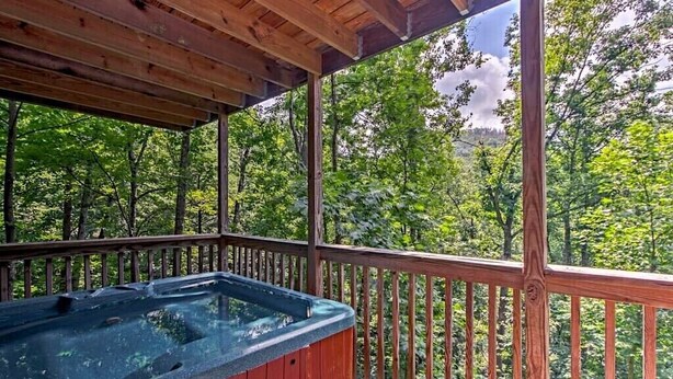 A wooden deck with a hot tub, surrounded by a wooden railing, overlooking a forested area. - Pappy’s Hideaway (Gatlinburg)