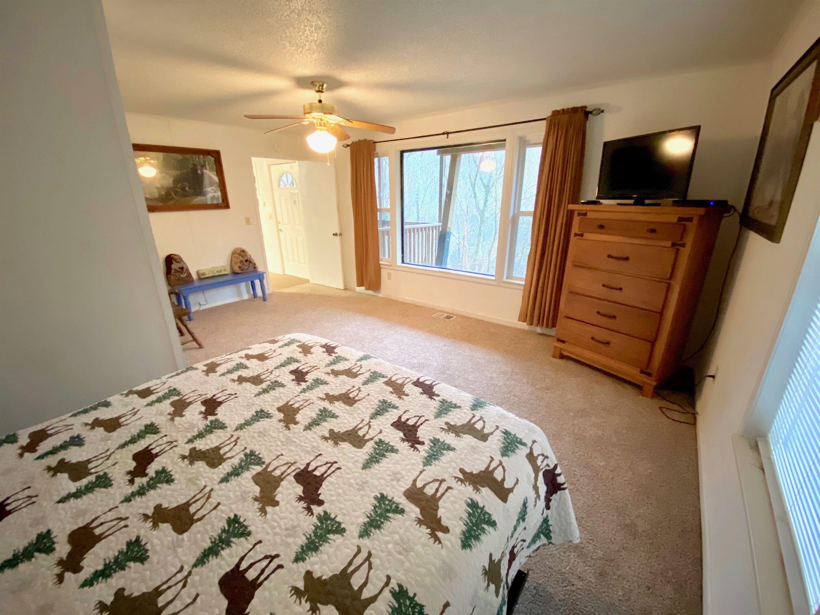 A bedroom with a bed, a dresser, a television, and a window with curtains.