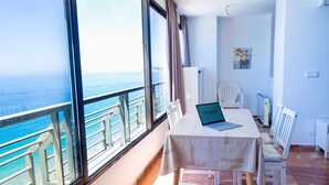A room with a large window overlooking the sea, a laptop on a table, and a chair.
