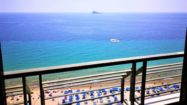 A beach view from a balcony with multiple levels of seating, clear blue water, and a distant island.