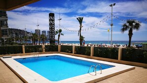 A rectangular swimming pool with a tiled border, surrounded by a low wall and a paved area.