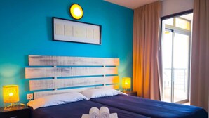 Ein Hotelzimmer mit einem großen Bett, zwei Nachttischlampen, einem gerahmten Bild an der Wand und einem Fenster mit Vorhängen.
