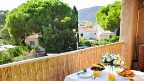 Un balcon avec une table mise pour le petit-déjeuner, comprenant des assiettes, un saladier de fruits et un vase de fleurs.