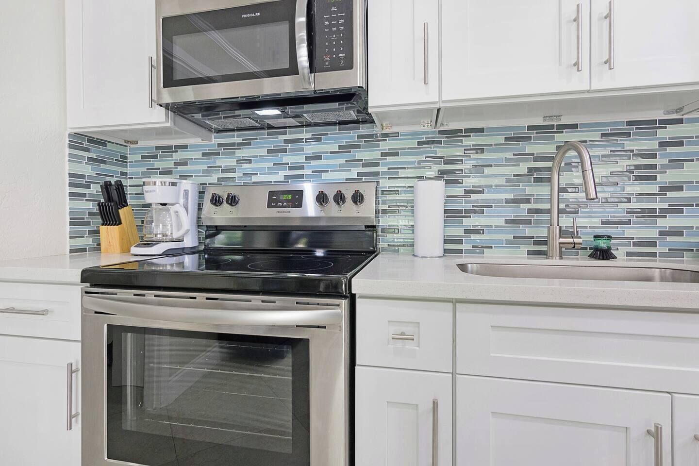 A kitchen with white cabinets, a stainless steel stove, a microwave, and a tiled backsplash.
