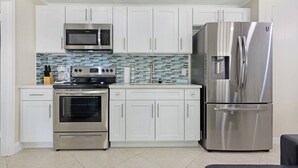 A modern kitchen with white cabinets, stainless steel appliances, a tiled backsplash, and a built-in oven.