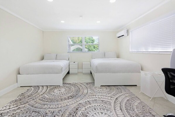 A bedroom with two beds, a patterned rug, a window with blinds, and an air conditioning unit. - Private Guest suite with a beautiful view of the new hard rock hotel and casino (Fort Lauderdale)