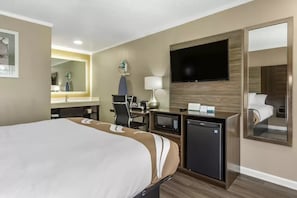 A hotel room with a large bed, a desk with a computer, a TV, and a mirror. - Quality Inn and Suites Pawleys Island SC (Pawleys Island)
