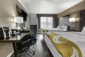 A hotel room with two beds, a desk with a lamp, a chair, a TV mounted on the wall, and a window with curtains. - Quality Inn and Suites Pawleys Island SC (Pawleys Island)