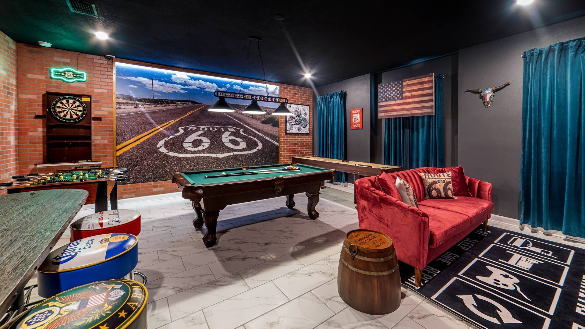 A room with a pool table, foosball table, dartboard, and a mural of Route 66.