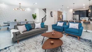 Una sala de estar moderna con un sofá gris, sillones azules y una mesa de centro de madera.