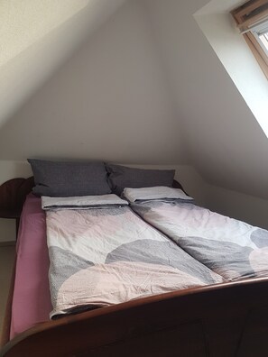 A bedroom with a sloped ceiling, a bed with a patterned bedspread, and a window.