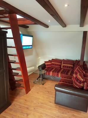 A living room with a wooden staircase, a glass coffee table, a sofa with patterned cushions, and a mounted television.