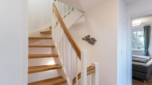 A staircase with wooden steps and white railings leading to a room with a grey sofa and a window with curtains.