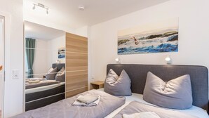 A bedroom with a bed, pillows, a nightstand, a mirror, and a painting on the wall.
