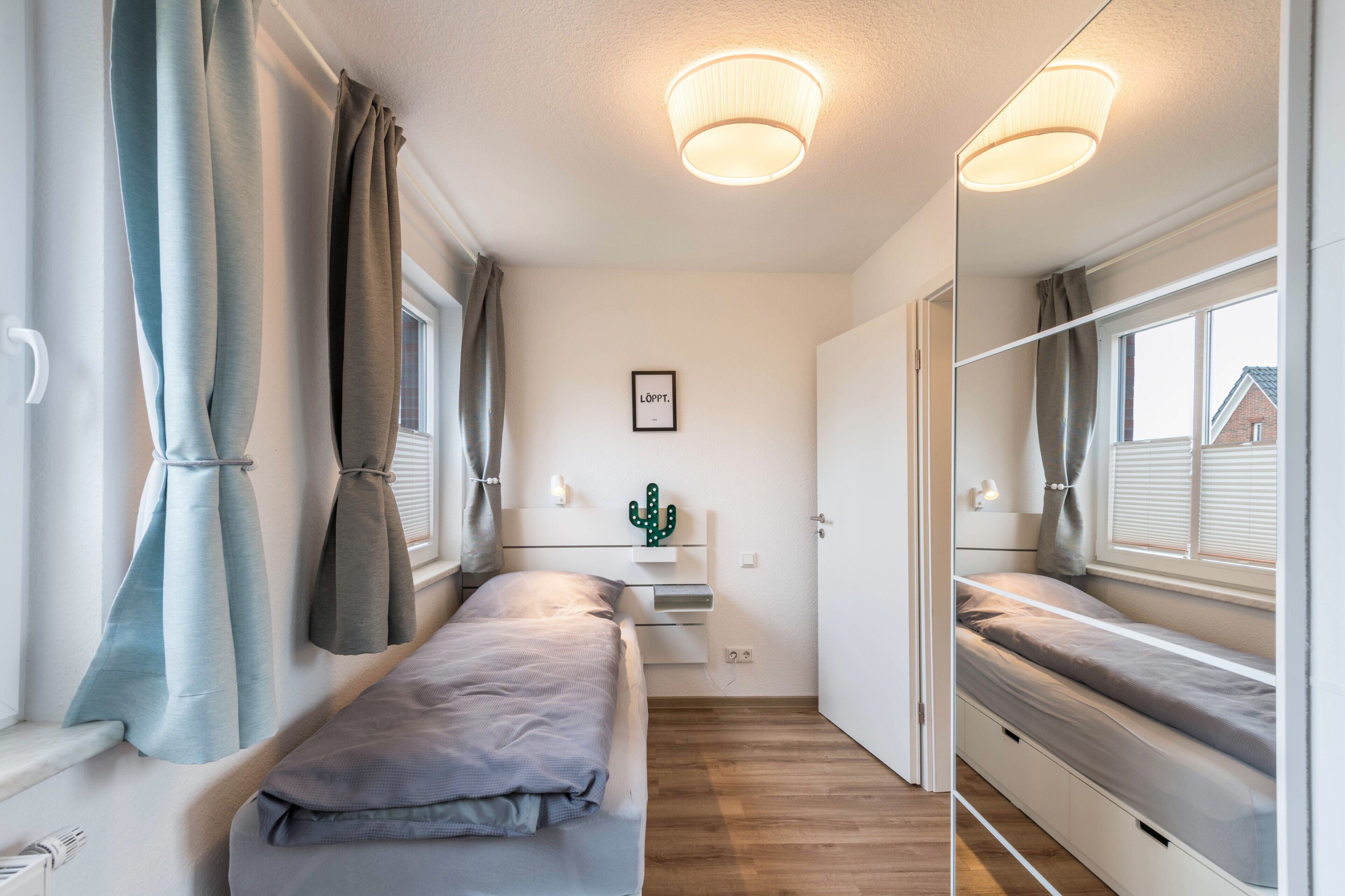 A compact bedroom with a bed, bedside tables, a cactus decoration, and a window with curtains.