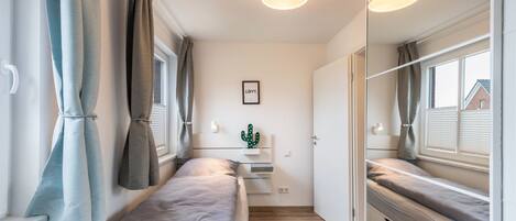 A compact bedroom with a bed, bedside tables, a cactus decoration, and a window with curtains.