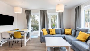 A modern living room with a grey sofa, yellow cushions, a white coffee table, and a flat-screen TV mounted on the wall.