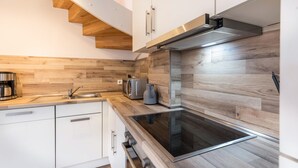 A modern kitchen with wooden flooring, white cabinets, a built-in oven, and a stainless steel range hood.