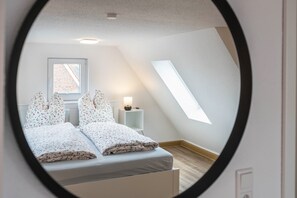 Quarto com cama, mesa de cabeceira, luminária, janela e claraboia.