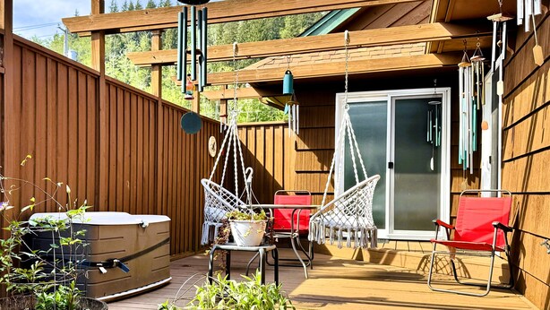 En træterrasse med jacuzzi, to hængestole og en rød stol.