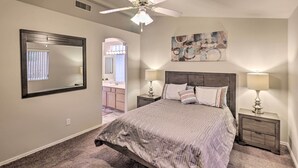 A bedroom with a large bed, two bedside tables with lamps, a ceiling fan, a large mirror, and a bathroom visible through an archway. - Fort Mohave Home w/ Hot Tub: 4 Mi to CO River! (Fort Mohave)