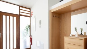 A modern room with a wooden floor, a wooden wardrobe, a white wall with a fire extinguisher, and a door with a wooden lattice.