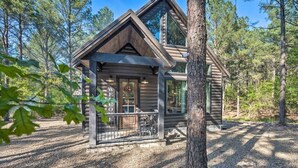 A log cabin with a porch and a large window, surrounded by trees.
