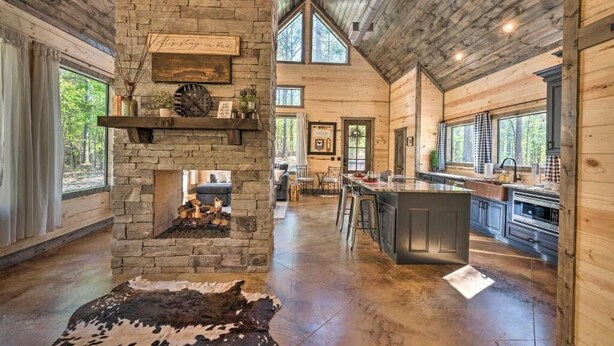 A spacious kitchen with a stone fireplace, wooden beams, and large windows.