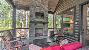 A log cabin with a stone fireplace, outdoor seating, and a view of the surrounding forest.