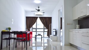 A modern hotel room with a dining area, a red sofa, a TV, and a kitchen area with white cabinets. - GT Home Cascades Residency (Petaling Jaya)