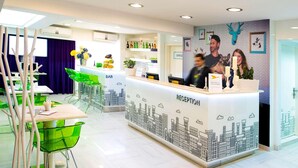 A modern reception area with a cityscape mural, a bar, and a reception desk. - Ibis Styles Skopje (Skopje)