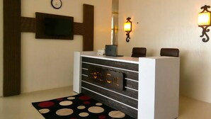 A reception desk with a digital clock, a flat-screen TV, and a laptop. There are two wall-mounted lights and a black and white patterned rug. - Hotel One DG Khan (Dera Ghazi Khan)