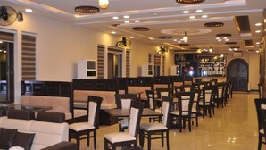 A restaurant with multiple dining tables and chairs, a bar area, and a seating area with sofas. - Hotel One DG Khan (Dera Ghazi Khan)