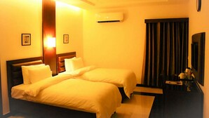 A hotel room with two beds, a ceiling fan, an air conditioning unit, a small table with a mirror, and a dark curtain. - Hotel One DG Khan (Dera Ghazi Khan)