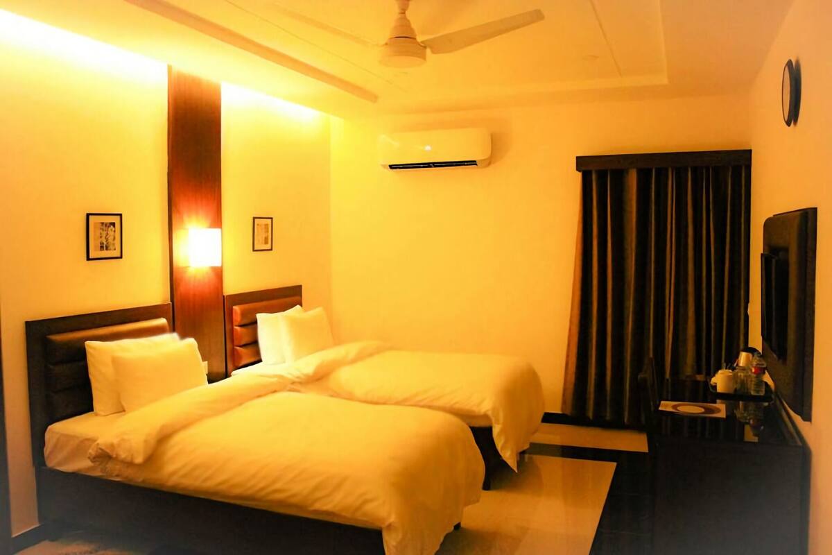 A hotel room with two beds, a ceiling fan, an air conditioning unit, a small table with a mirror, and a dark curtain.