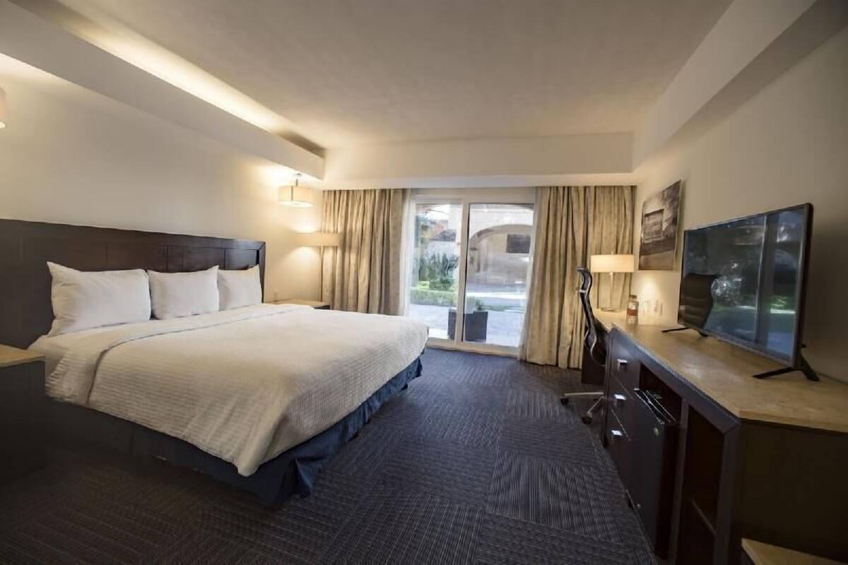 A hotel room with a bed, a desk, a television, and a view of the outdoors.