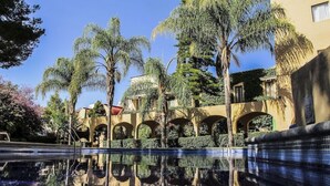 Una piscina con reflejos nítidos, rodeada de palmeras y un edificio con arcos.