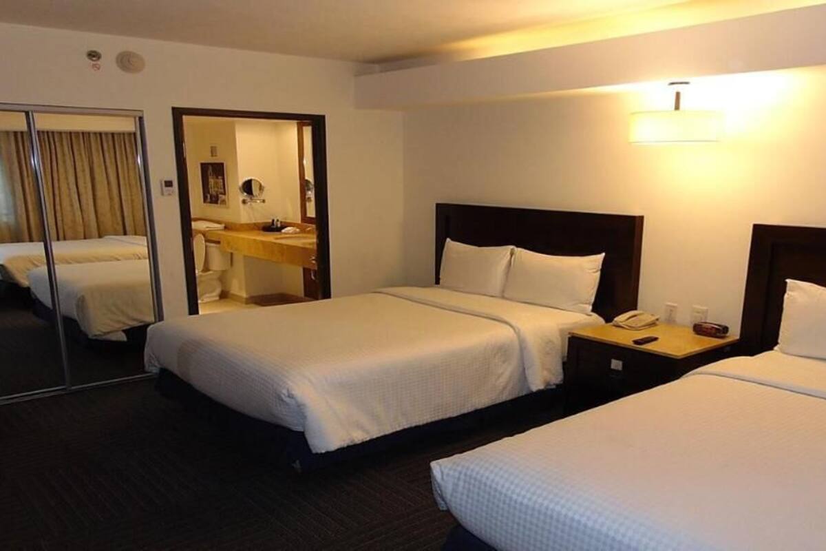 A hotel room with two beds, a mirror, a desk, and a bathroom visible through a sliding door.