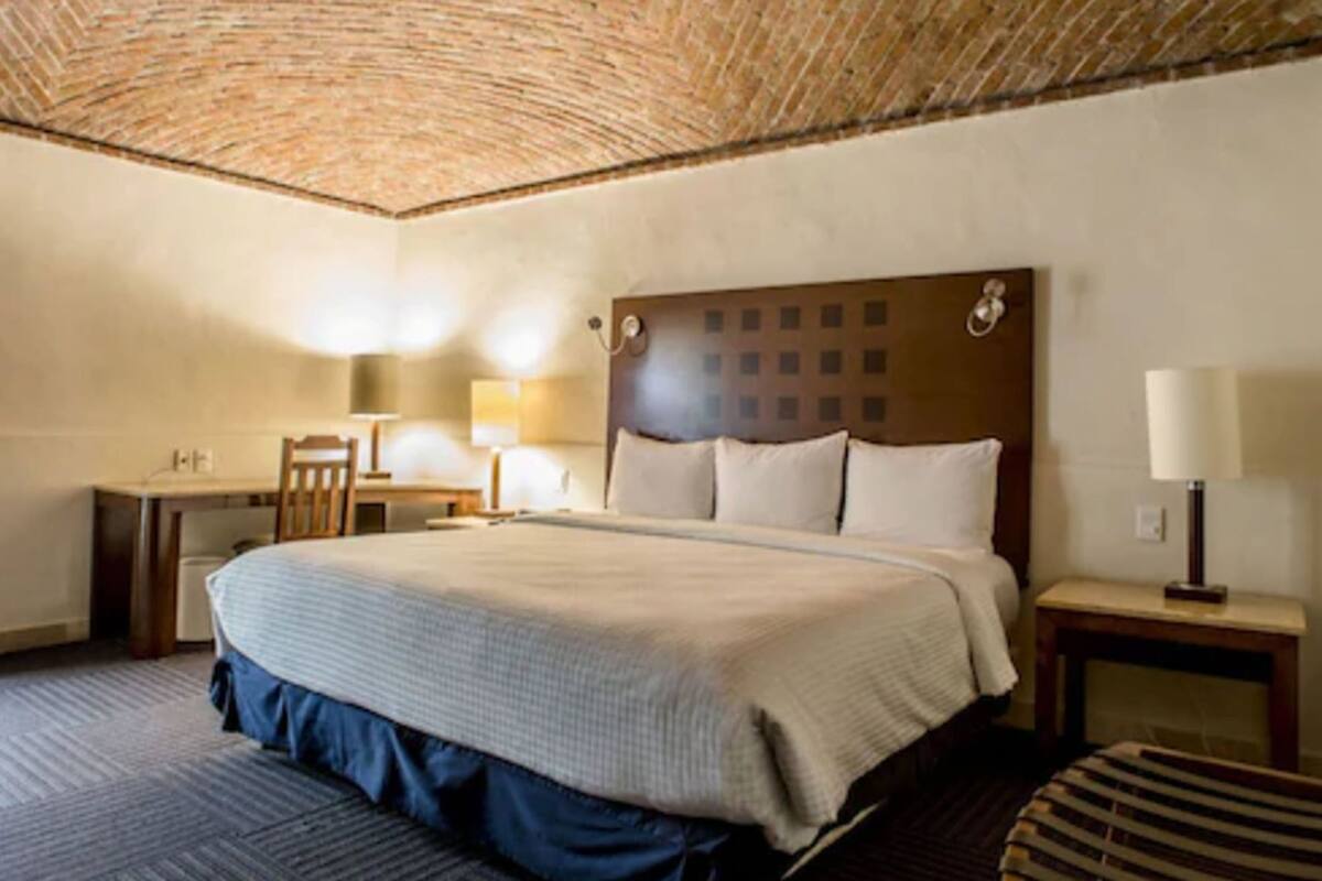 A hotel room with a large bed, a desk, a chair, and a lamp.
