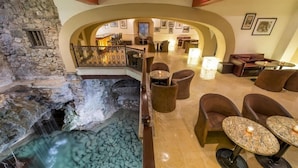 Vestíbulo de hotel con pared de piedra, una cascada ornamental y zonas de estar con mesas y sillas.