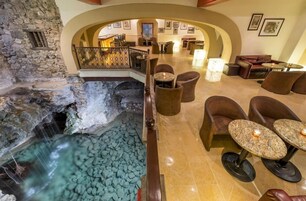 Vestíbulo de hotel con pared de piedra, una cascada ornamental y zonas de estar con mesas y sillas.